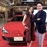 a man and woman standing next to a red ferrari sports car