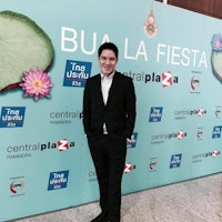 a man in a suit standing in front of a banner that says bu la fiesta